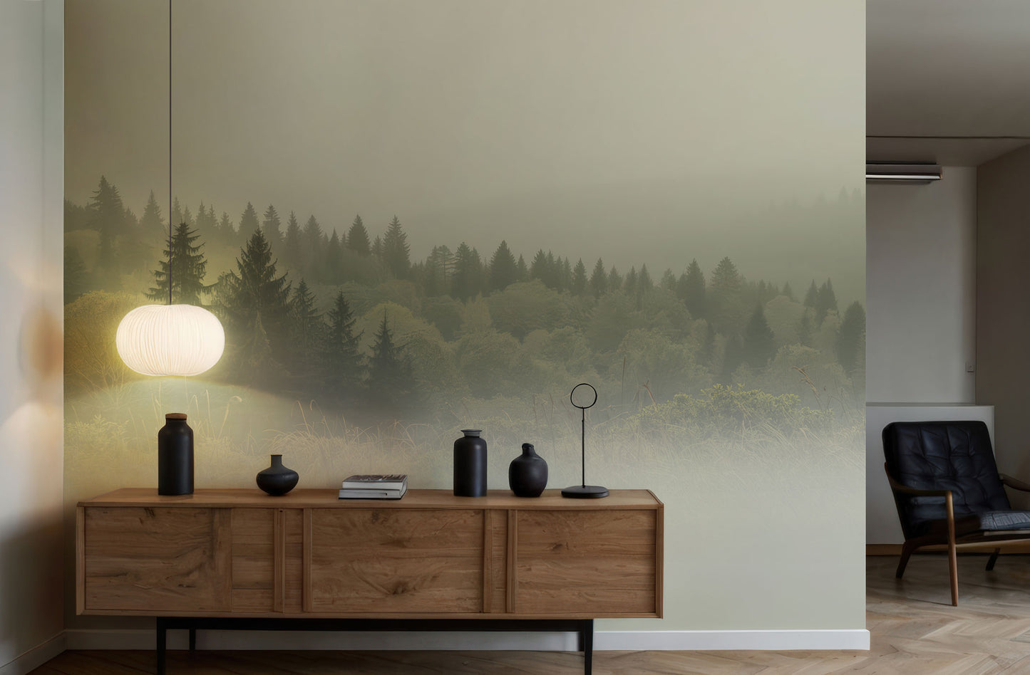 Holzsideboard mit schwarzen Vasen, Büchern und einem weißen Lampenschirm vor einer Wand mit Waldtapete von Superwalls, daneben ein schwarzer Ledersessel.