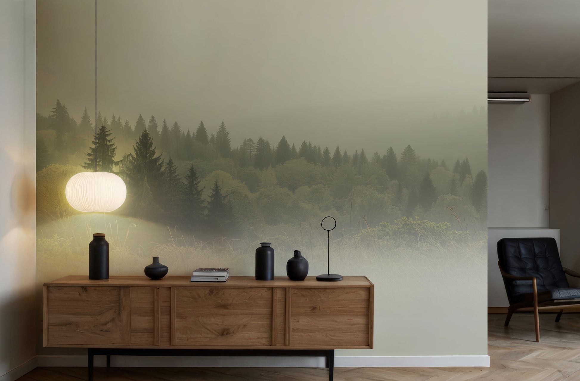 Holzsideboard mit schwarzen Vasen, Büchern und einem weißen Lampenschirm vor einer Wand mit Waldtapete von Superwalls, daneben ein schwarzer Ledersessel.