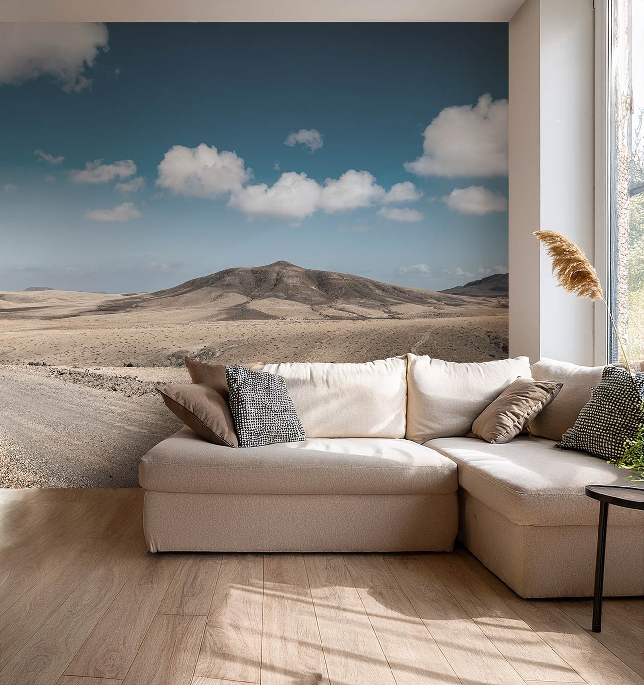 Beige Ecksofa mit mehreren Kissen vor einer Wand mit einer Fototapete Wüstenlandschaft unter blauem Himmel mit Wolken von Superwalls.