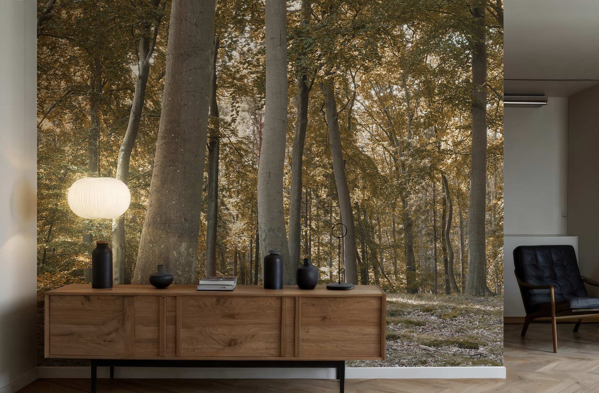 Holzsideboard mit Dekoration vor einer Wandtapete mit Waldmotiv von Superwalls, daneben ein schwarzer Sessel in einem modernen Raum.