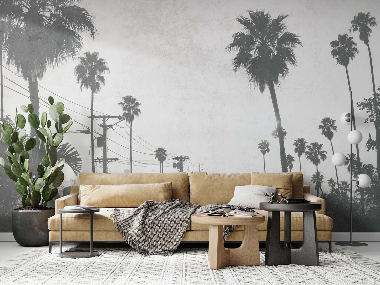Beige Sofa mit Kissen und kariertem Plaid vor einer Wand mit schwarz-weißer Fototapete von Palmen und Stromleitungen von Superwalls, daneben großer Kaktus und zwei runde Couchtische