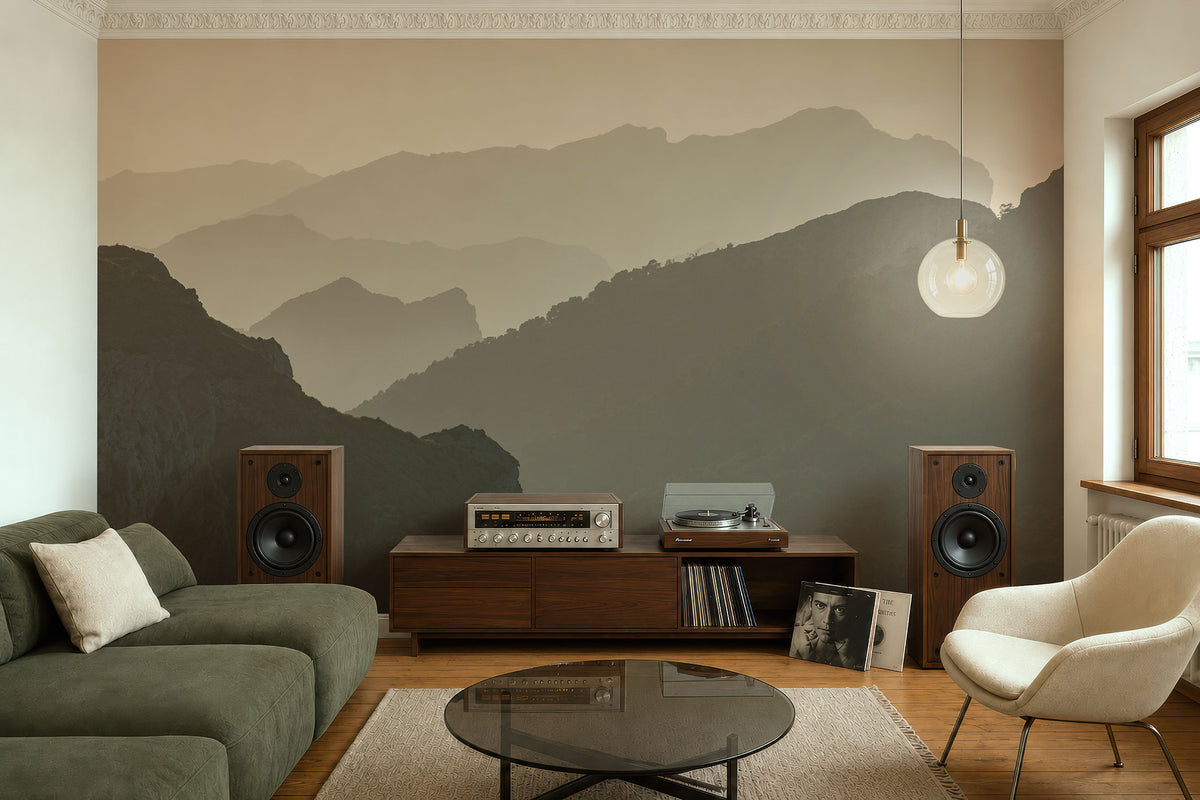 Wohnzimmer mit braunem Holzsideboard, zwei Lautsprechern, Plattenspieler, grünem Sofa, beigem Sessel, rundem Glastisch und einer Tapete mit Bergsilhouetten von Superwalls