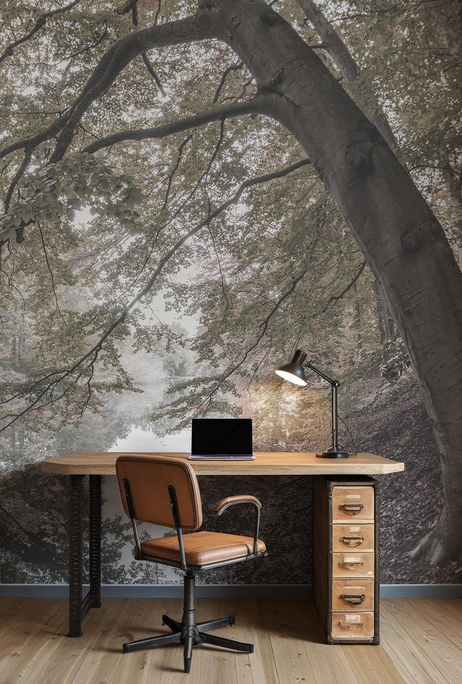 Schreibtisch mit Stuhl, Laptop und Schreibtischlampe vor einer Wand mit großflächigem Waldfototapete von Superwalls