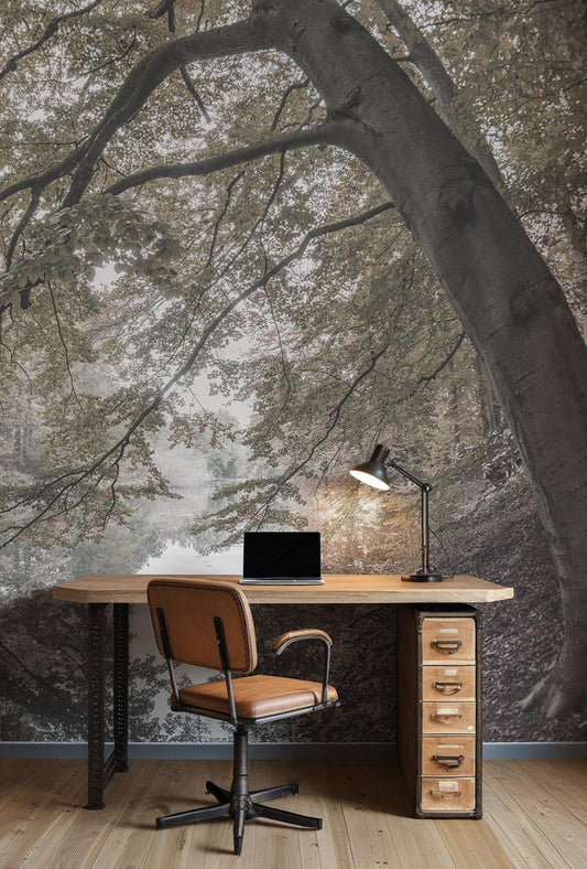 Schreibtisch mit Stuhl, Laptop und Schreibtischlampe vor einer Wand mit großflächigem Waldfototapete von Superwalls