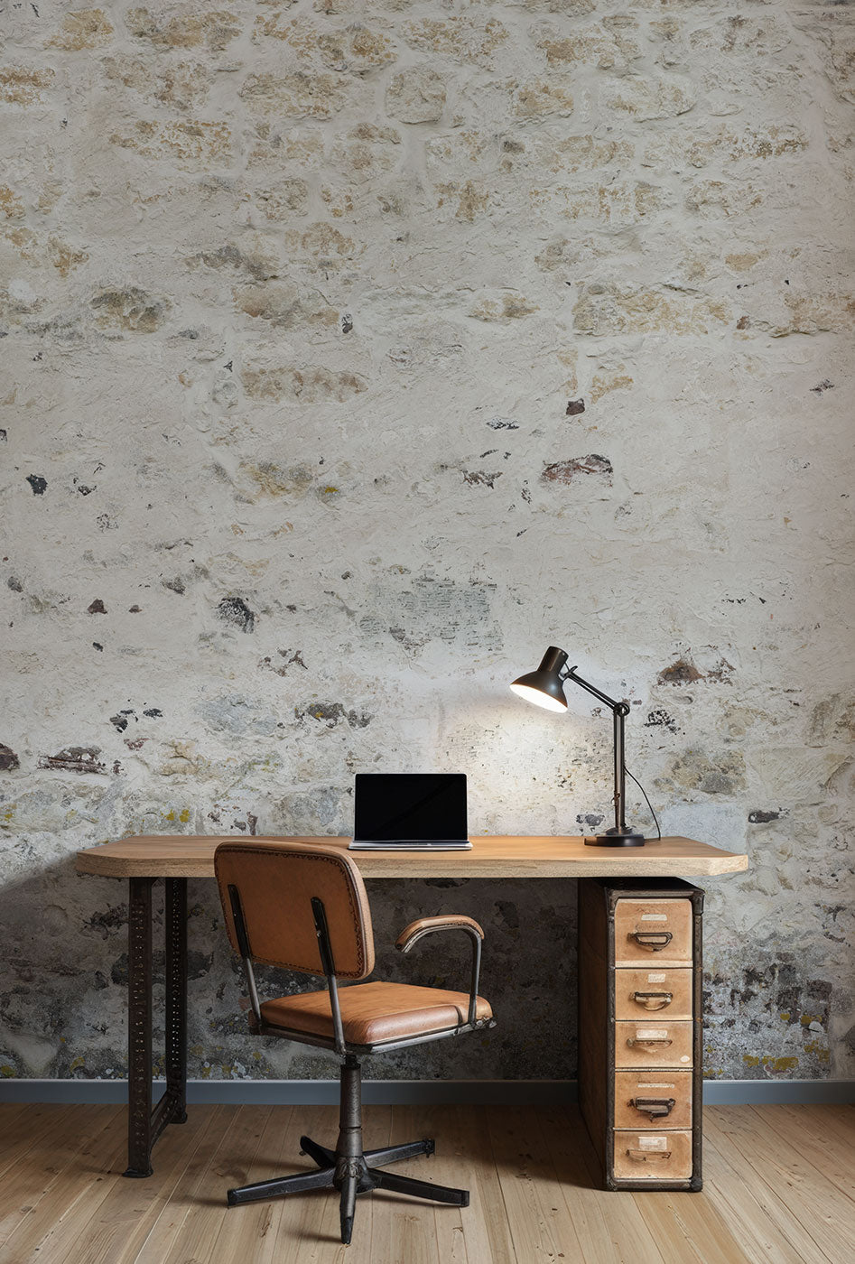 Schreibtisch mit Laptop, verstellbarer Schreibtischlampe und braunem Drehstuhl vor einer rauen Steinwand-Tapete von Superwalls